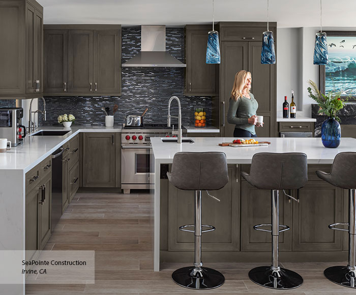 woman walking through kitchen with dark gray cabinet and dark blue backsplash